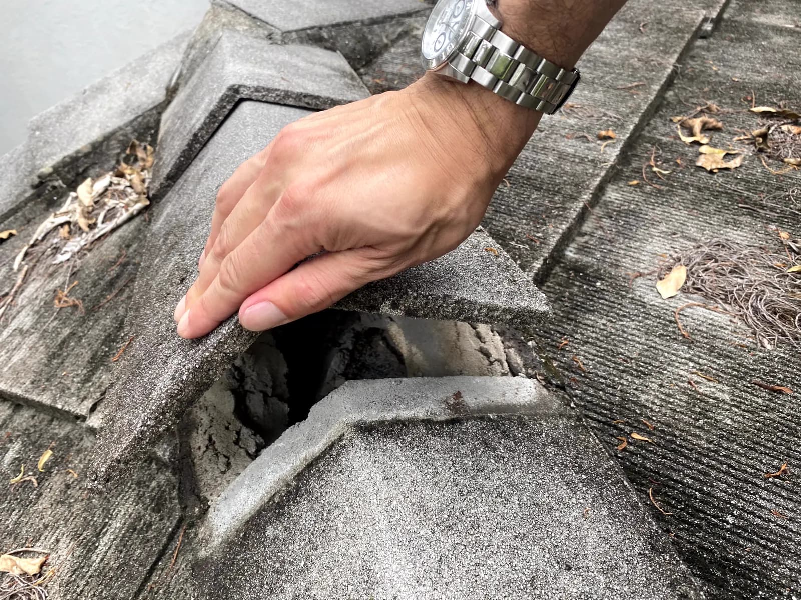 Adjuster's hand lifting a cracked ridge cap tile to expose the void beneath during a roof inspection