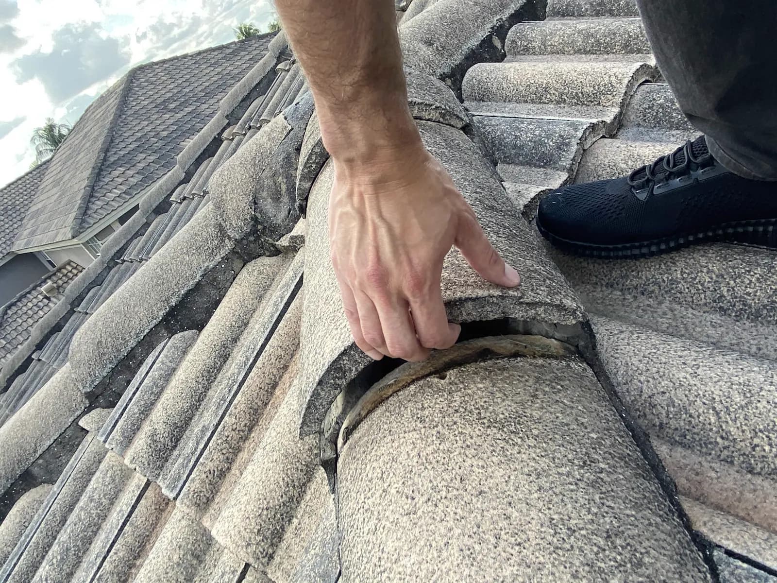 Adjuster on a tile roof lifting a loose ridge cap to reveal the gap and failed bedding underneath