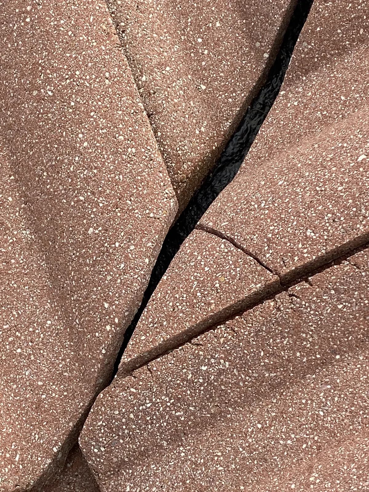 Close-up of a concrete roof tile split by a wide open fracture with branching cracks