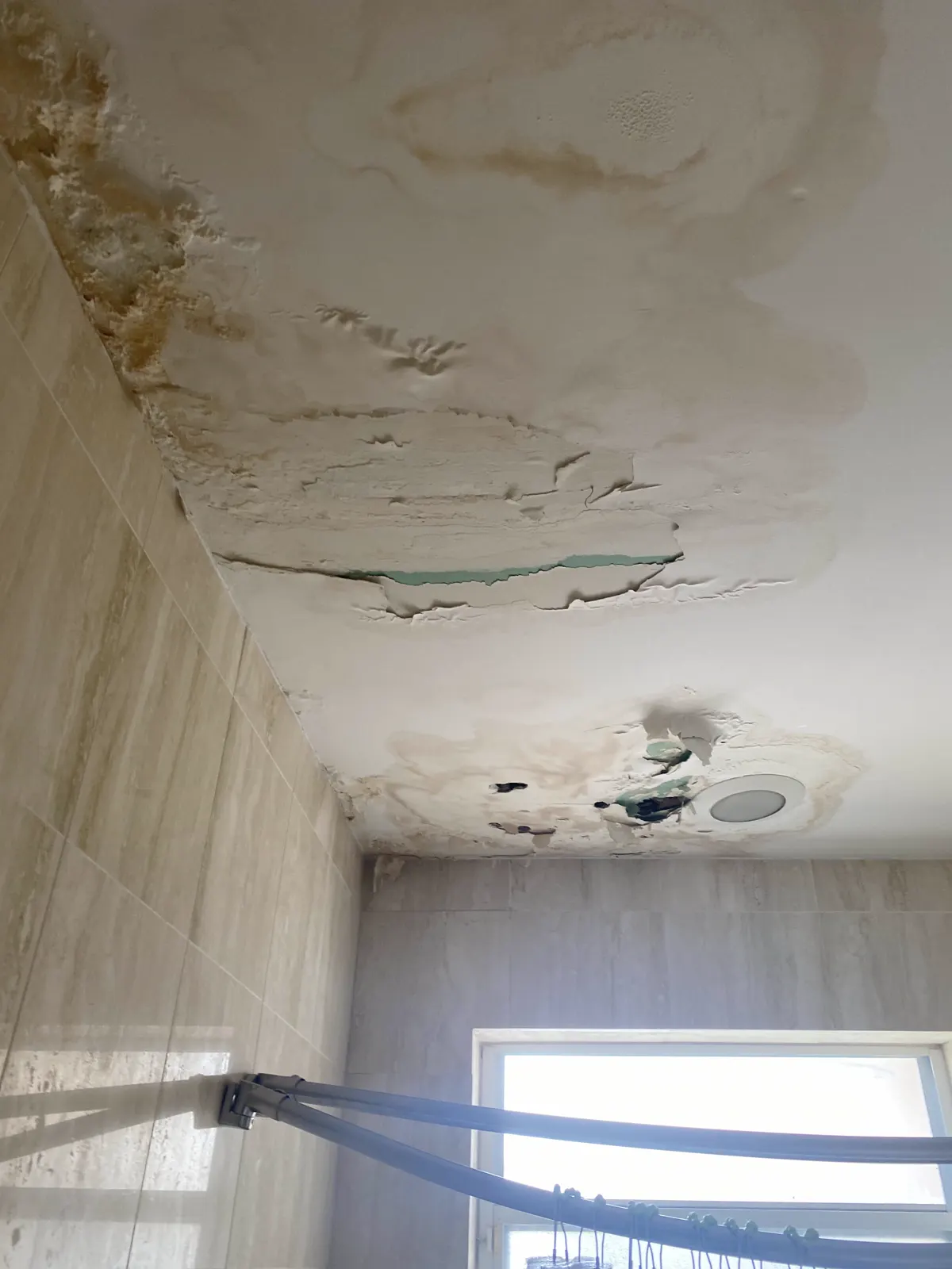 Bathroom ceiling with water stains, peeling paint and bubbling drywall tape around the light fixture
